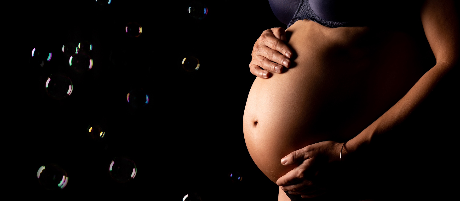 Ausschnitt eines Babybauches vor schwarzem Hintergrund mit Seifenblasen