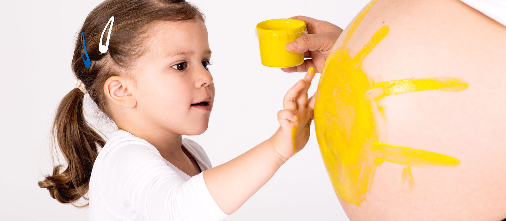 Ein Mädchen bemalt den schwangeren Bauch der Mutter mit einer großen gelben Sonne