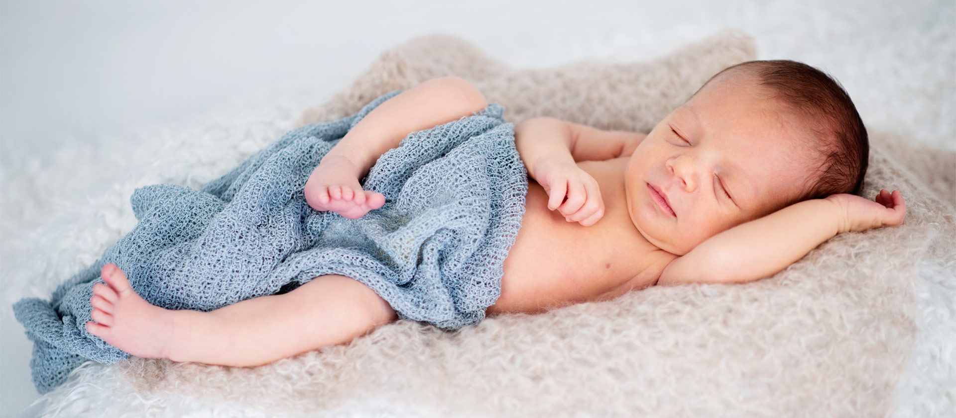 Ein Baby liegt auf einem Fell mit einem blauen Tuch und schläft
