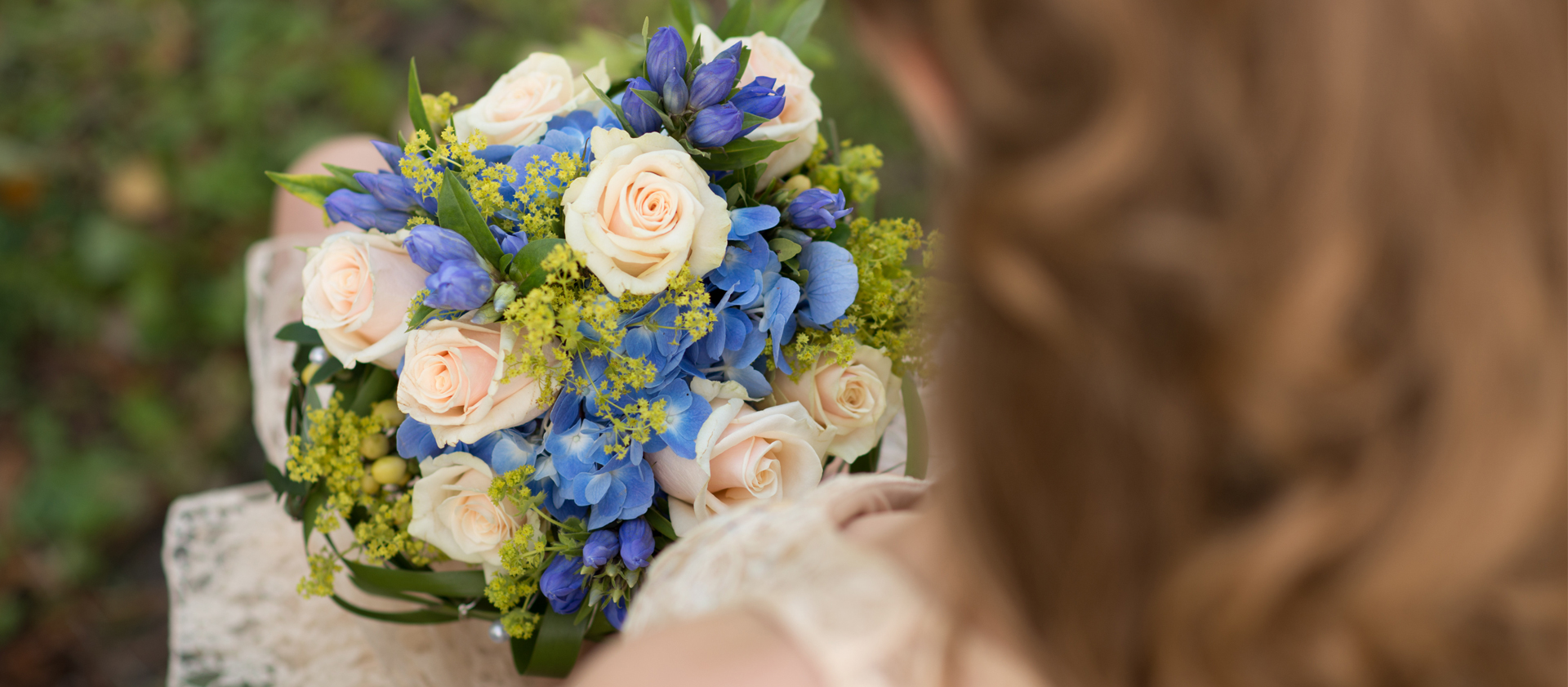 Eine Braut hällt ihren beige-blauen Hochzeitsstrauss im Arm