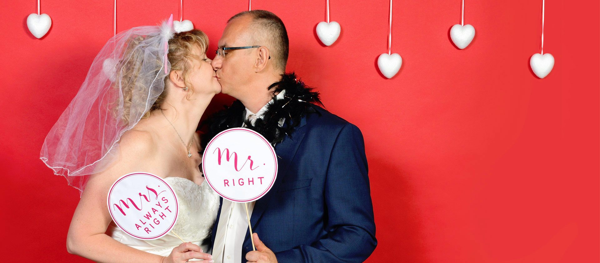 Ein Brautpaar küsst sich in einem Photobooth und hält dabei Schilder Mr. Right und Mrs. Always Right