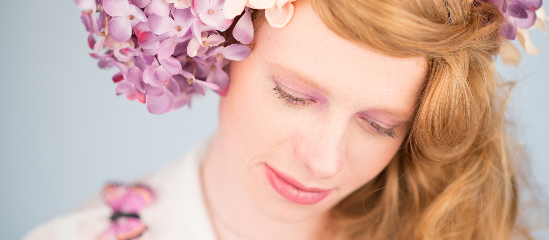 Mädchen mit einem Blumenkranz im Haar und Schmetterling auf der Schulter